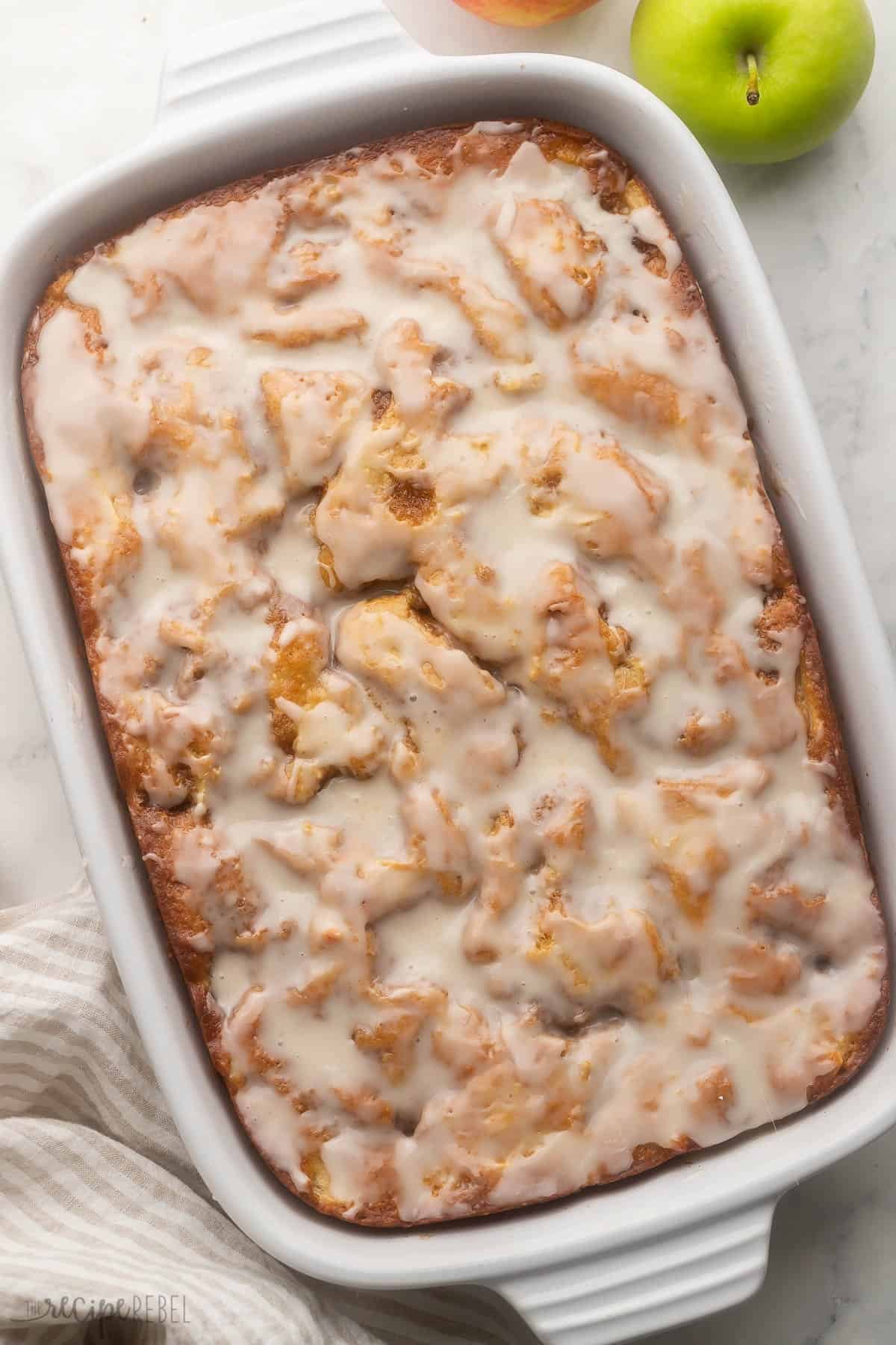 grosse plaque blanche de gâteau de beignets aux pommes avec des pommes à côté.