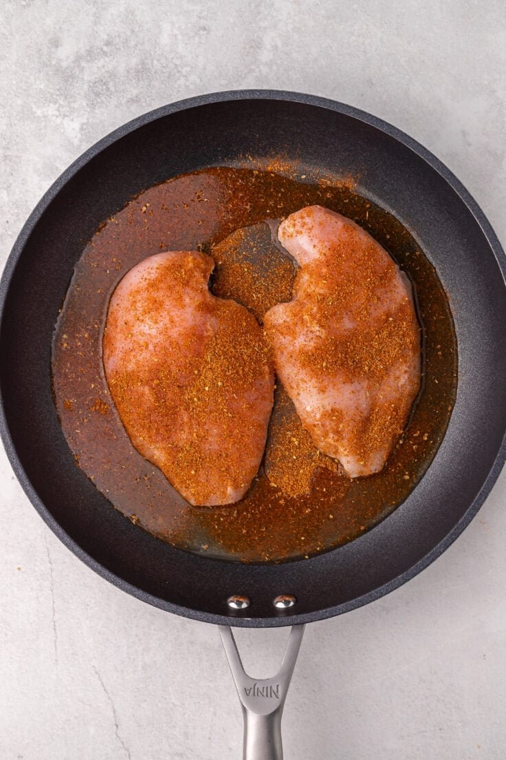 poêle noire avec deux poitrines de poulet assaisonnées à l'intérieur.