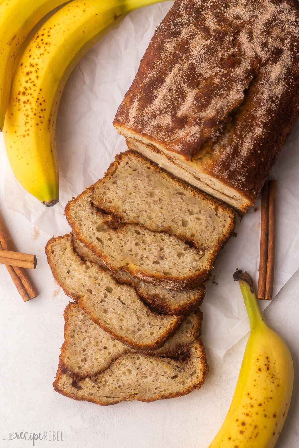 vue aérienne du pain à la banane à la cannelle sur du papier parchemin avec des bananes à côté.