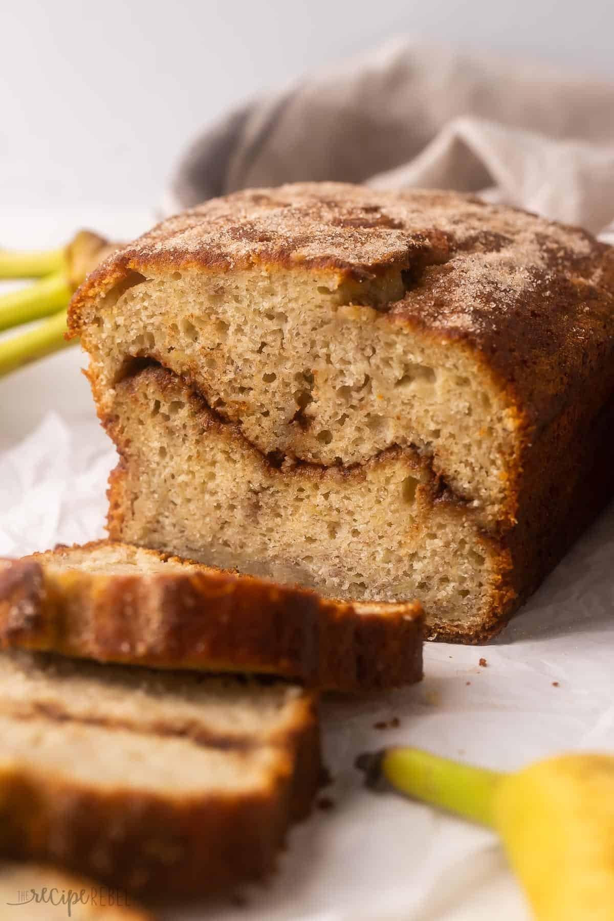 chleb à la banane à la cannelle tranché sur papier parchemin avec des bananes à côté.