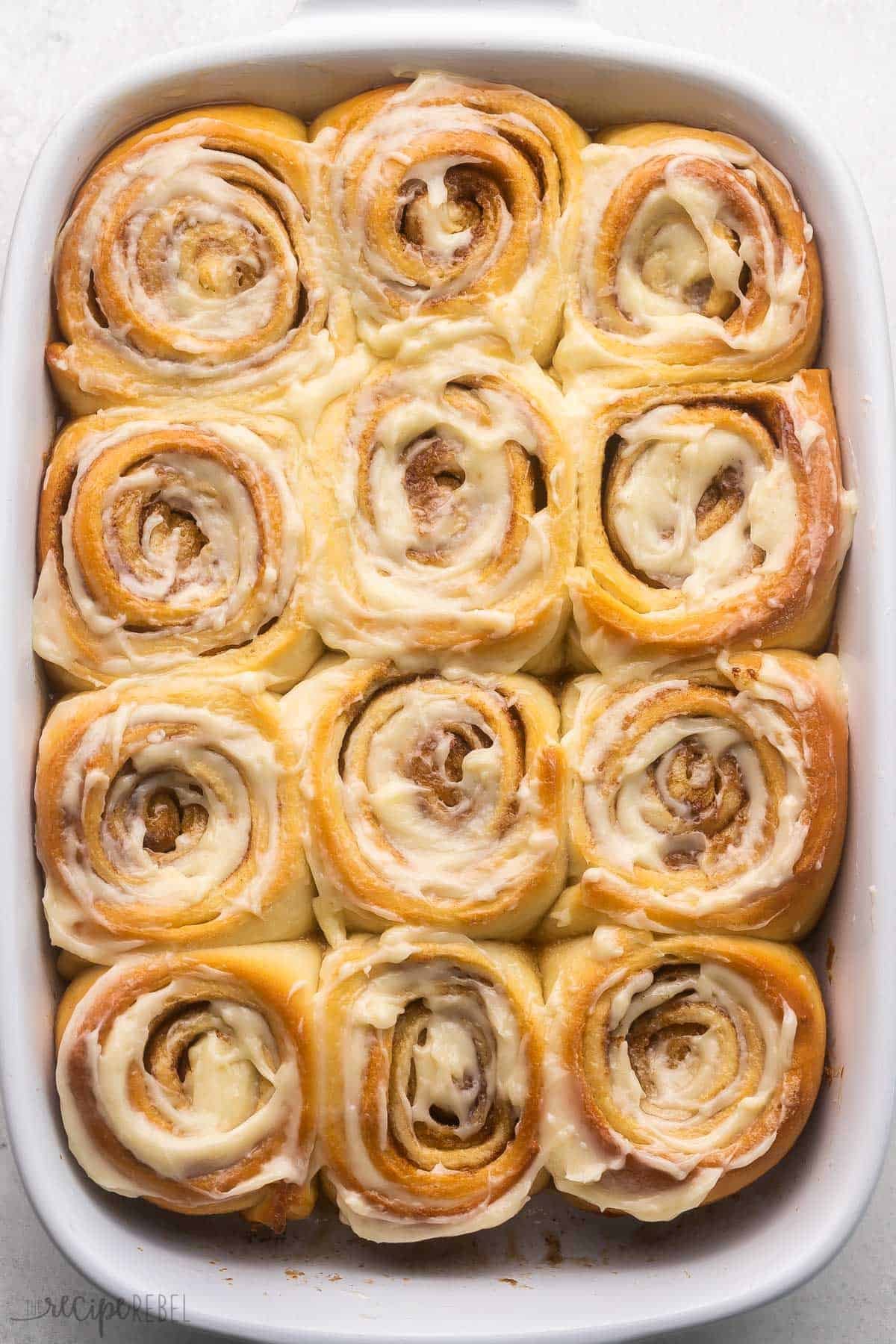 une plaque de brioches à la cannelle avec un glaçage sur le dessus.