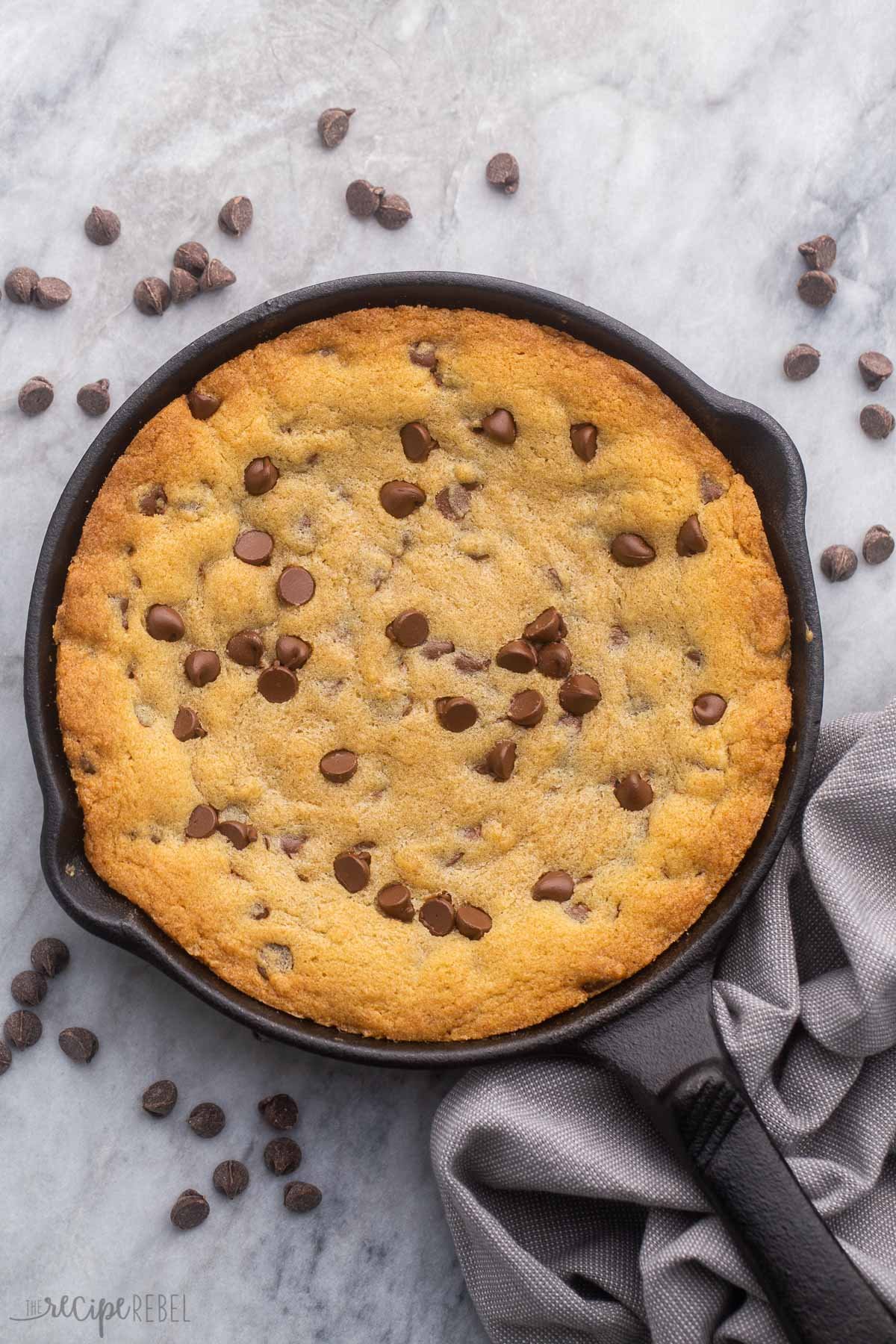 vue aérienne d'un cookie cuit dans une poêle entouré de pépites de chocolat.