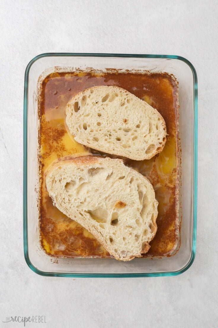deux morceaux de pain posés dans un plat en verre avec les ingrédients humides pour le pain perdu.