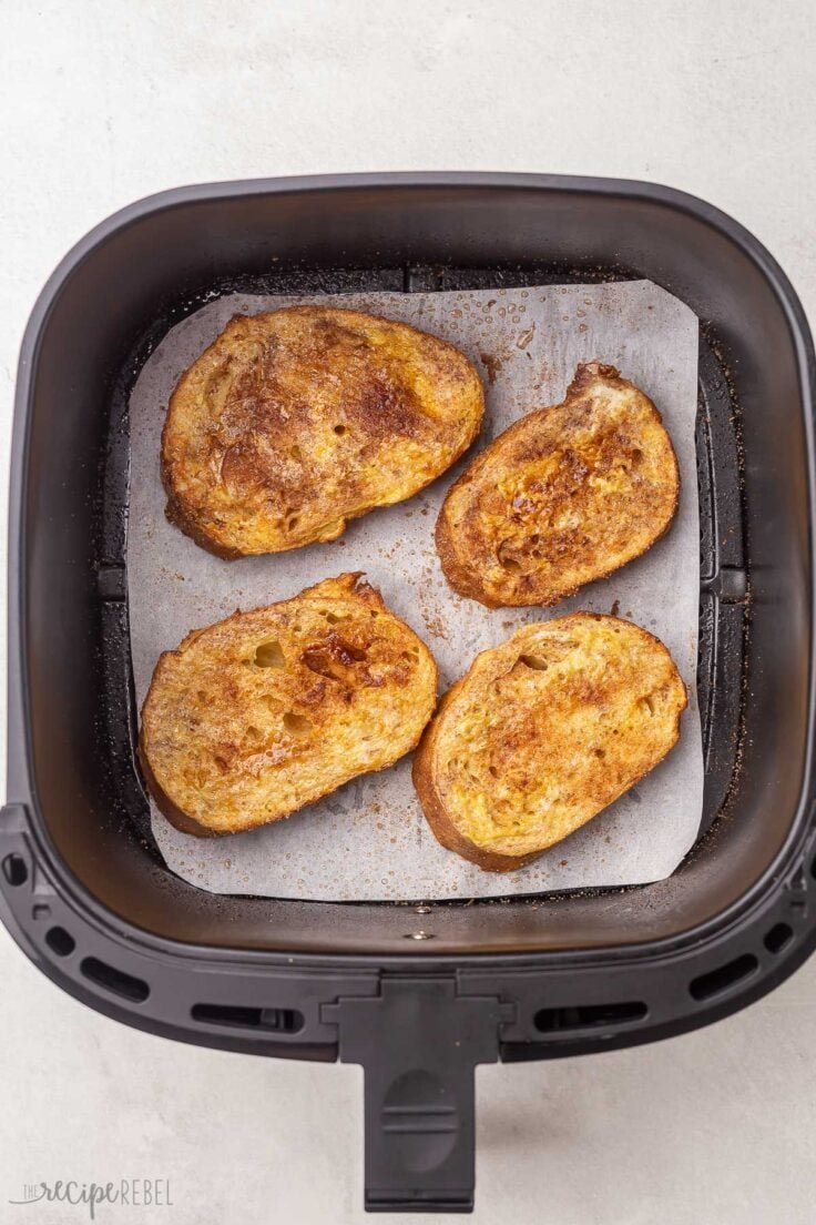 quatre morceaux de pain perdu frits reposant sur du papier sulfurisé dans le panier de la friteuse à air.