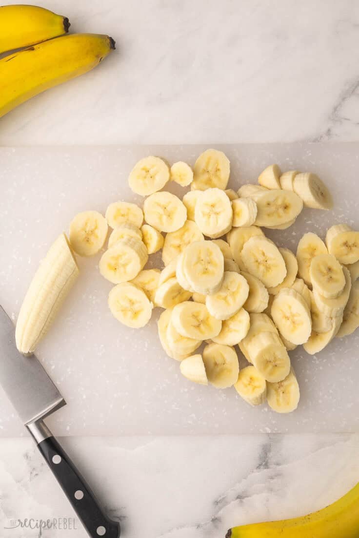 Bananes tranchées sur une planche à couper avec un couteau à côté.