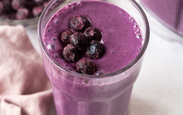 smoothie aux bleuets dans un grand verre avec des bleuets congelés sur le dessus