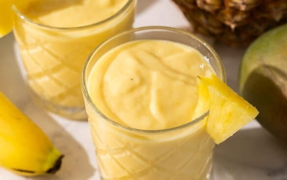 verres de smoothie tropical avec ananas et mangue à côté.