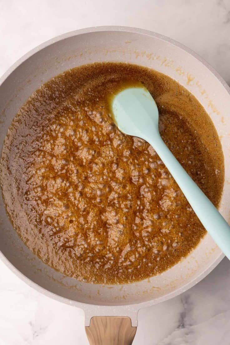 Poêle avec du caramel fondu et une spatule bleue.