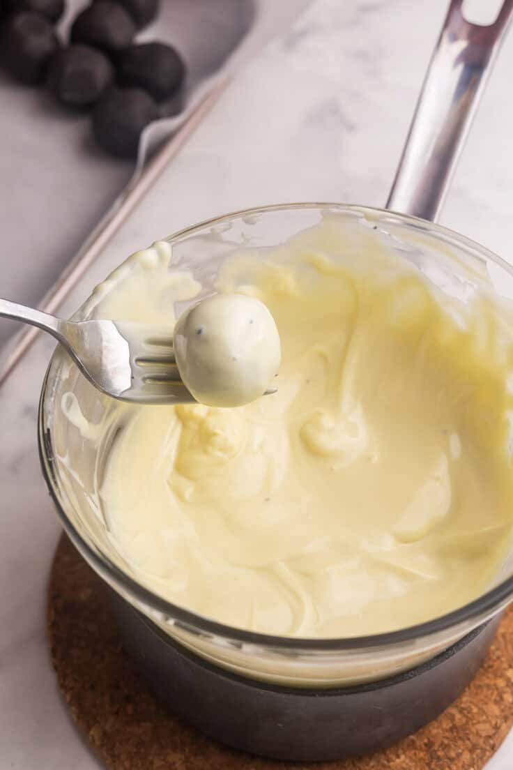 a fork holding an oreo ball over a bowl of melted white chocolate.