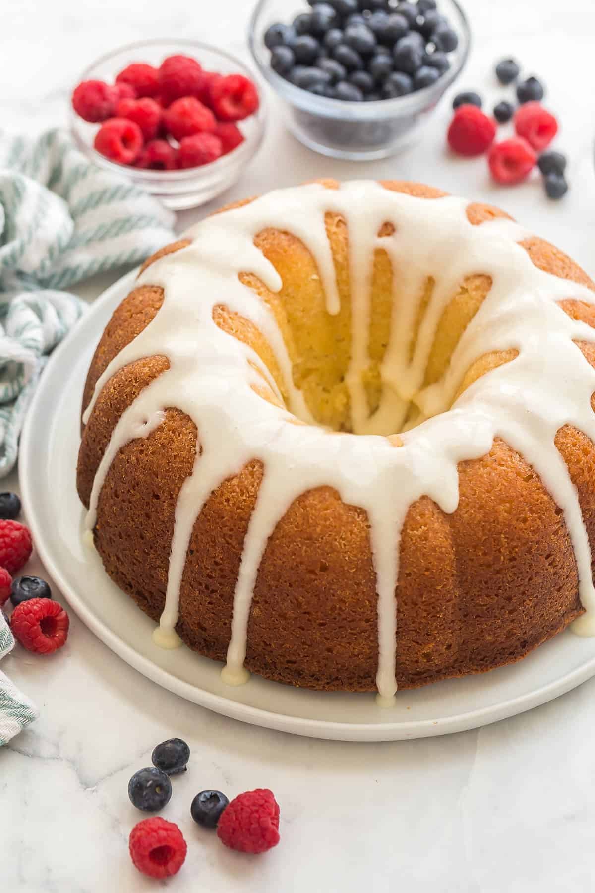 gâteau bundt au citron avec glaçage au citron sur une assiette blanche avec des baies autour.