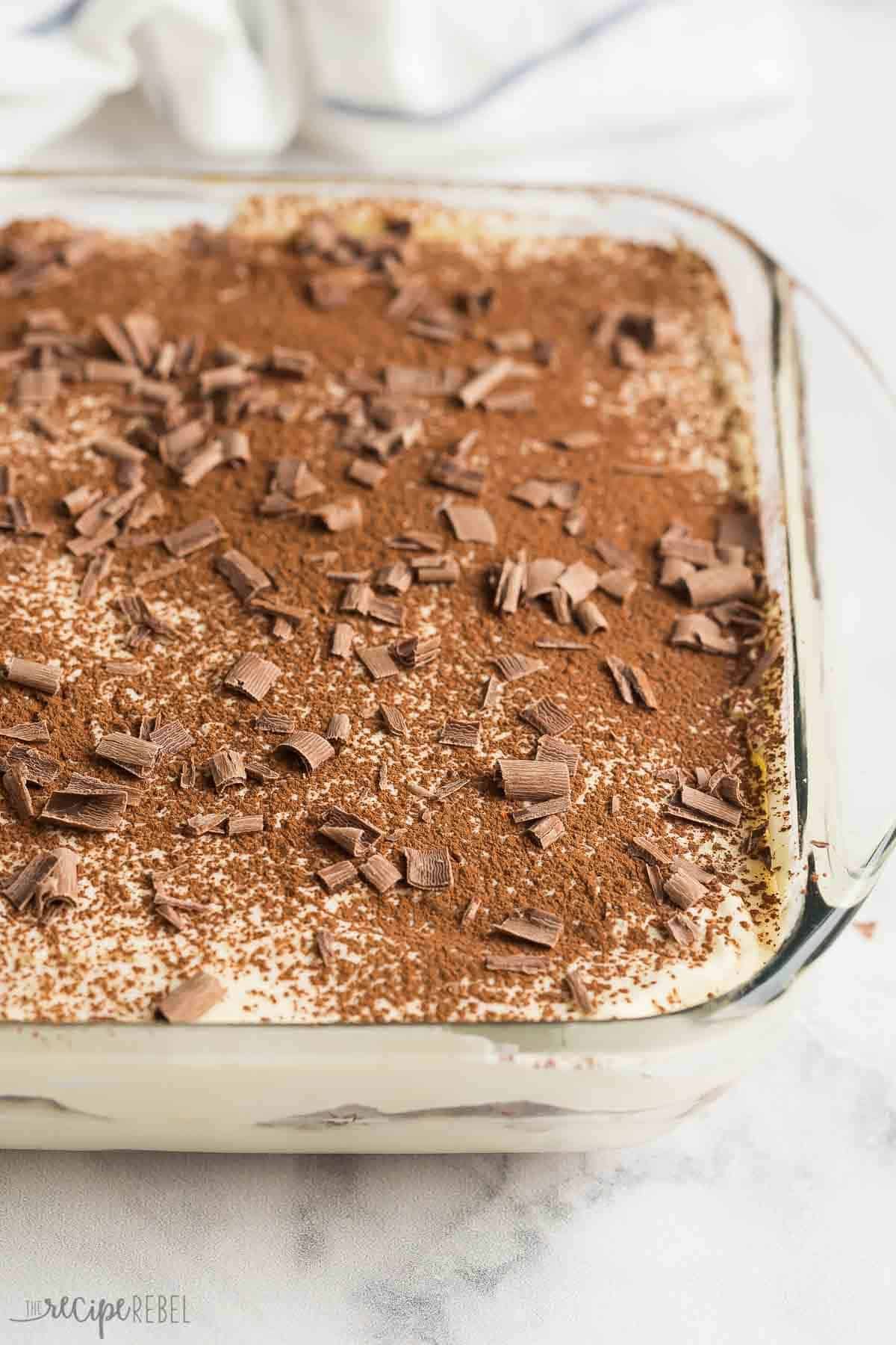 Un plat complet de tiramisu avec du cacao en poudre et des copeaux de chocolat sur le dessus.