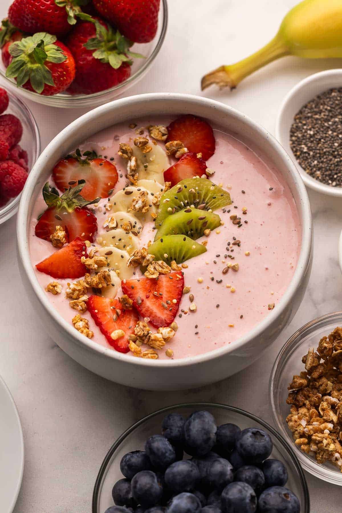 bol de smoothie aux fraises avec des fraises tranchées, bananes et kiwi ainsi que du granola.