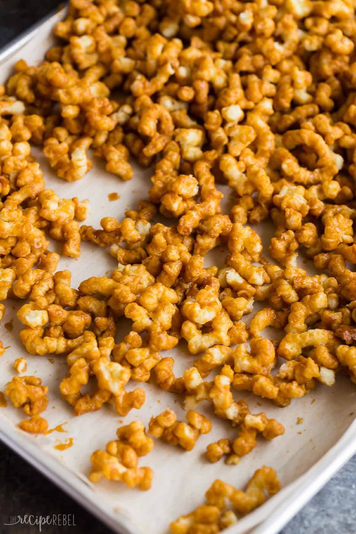 Caramel puff corn étalé sur une plaque de cuisson tapissée de papier sulfurisé.