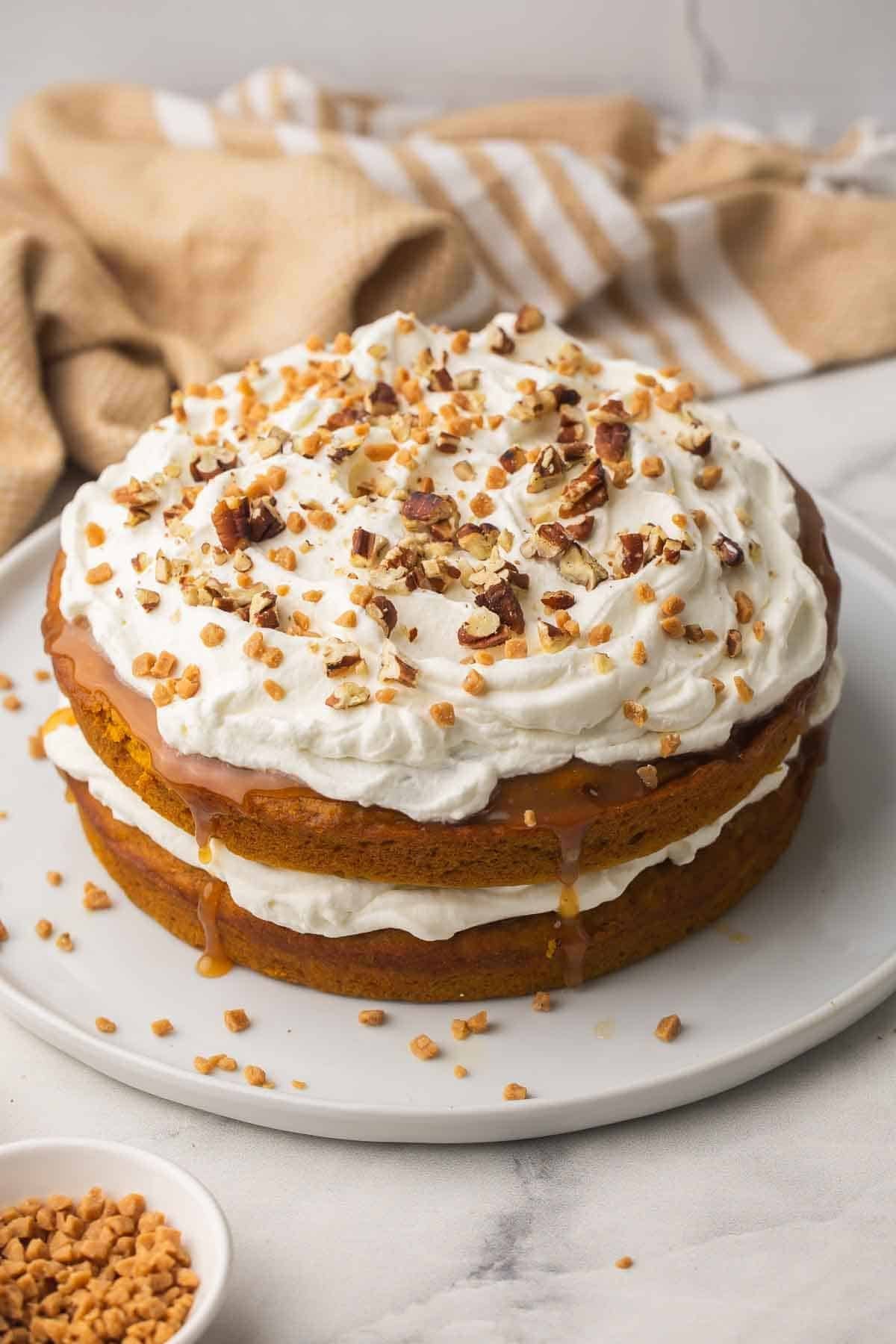 gâteau à la citrouille, caramel et noix de pécan sur une grande assiette blanche avec des morceaux de caramel à côté.