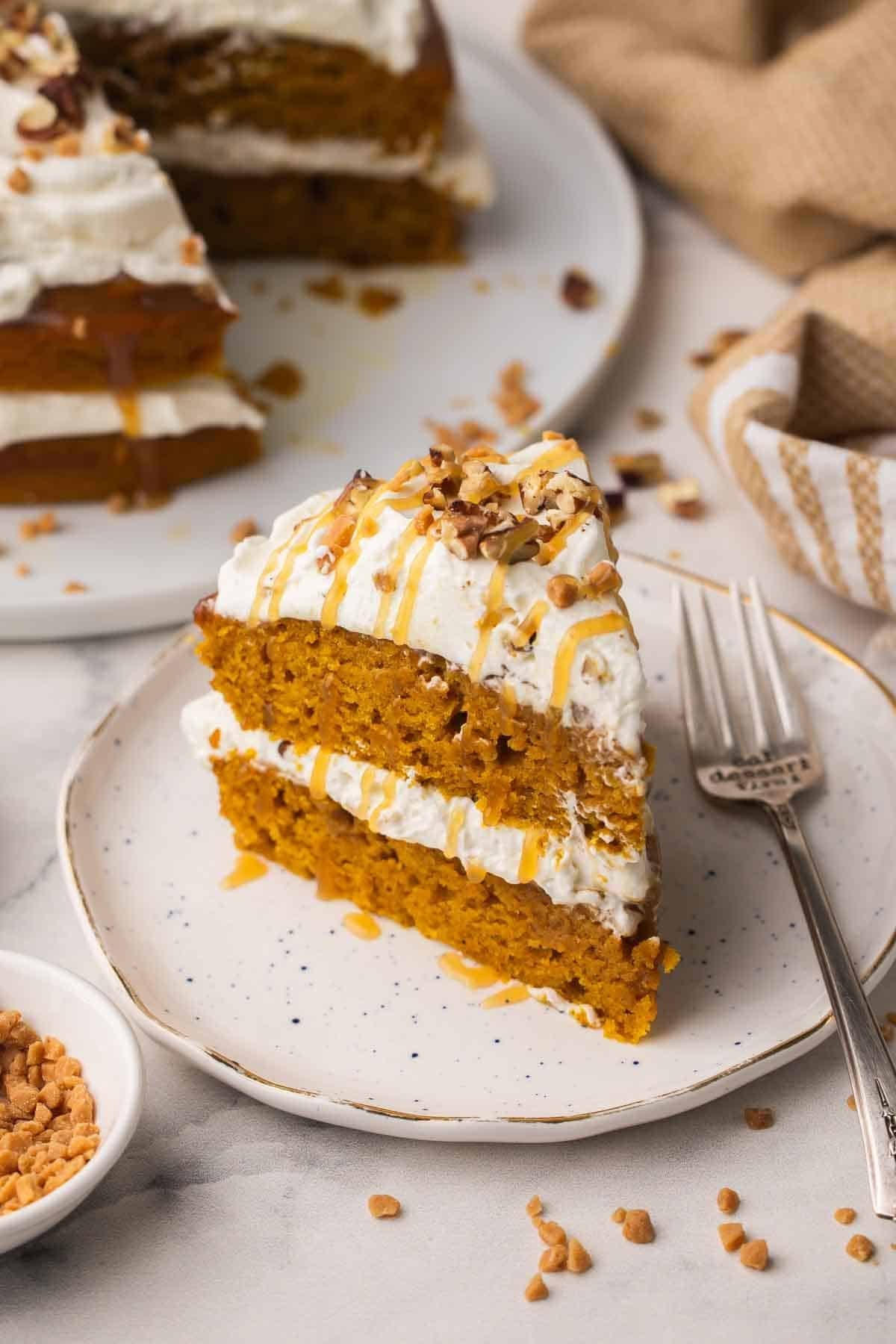 une tranche de gâteau à la citrouille, caramel et noix de pécan sur une assiette speckled.