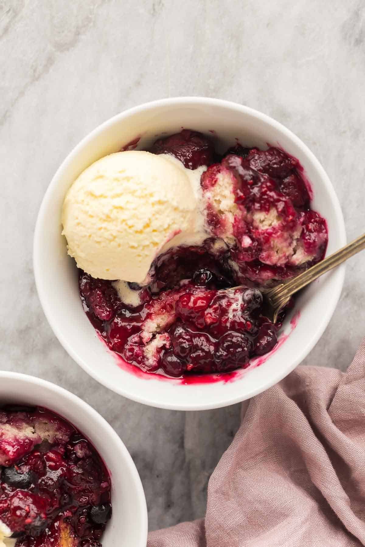 Deux bols de crumble aux baies avec de la crème glacée à côté d'une serviette en lin rose.