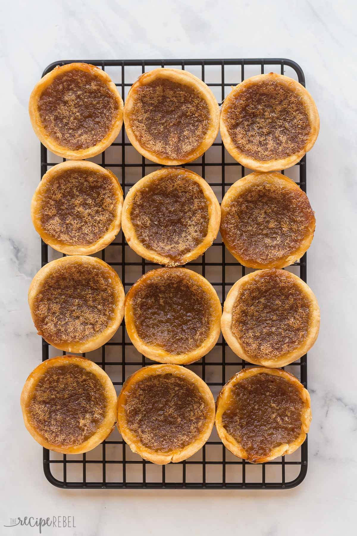 Ces Tartelettes au Beurre sont un classique canadien qui se prépare en seulement 25 minutes ! Des coques de pâtisserie maison sont remplies d'une garniture riche, au sucre brun (raisins en option !), puis cuites jusqu'à ce qu'elles soient beurrées et feuilletées à l'intérieur et gooey à l'intérieur. tartelettes au beurre finies sur un grille noire
