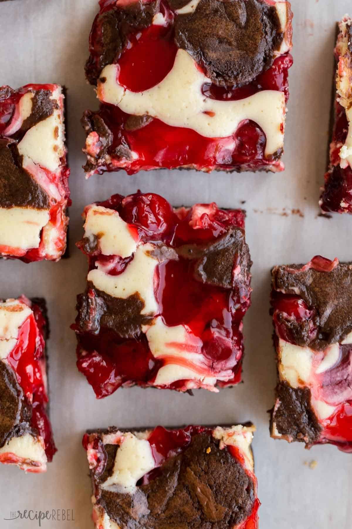 Rangées de brownies au cheesecake aux cerises disposés sur du papier sulfurisé blanc.