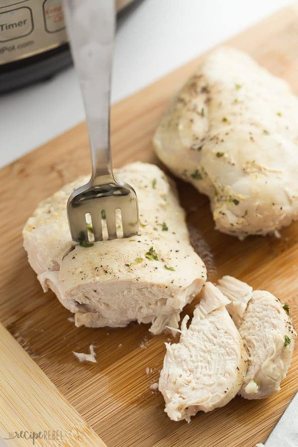 C'est la MEILLEURE façon de cuire des poitrines de poulet congelées dans l'Instant Pot ! C'est tellement facile et elles s'en sortent si bien que je ne prends presque jamais le temps de décongeler le poulet avant de le cuire. Ajoutez des assaisonnements, des sauces, un bouillon, ou juste de l'eau, du sel et du poivre, et le résultat est toujours incroyable. poitrines de poulet sur une planche à découper en train d'être tranchées devant l'Instant Pot