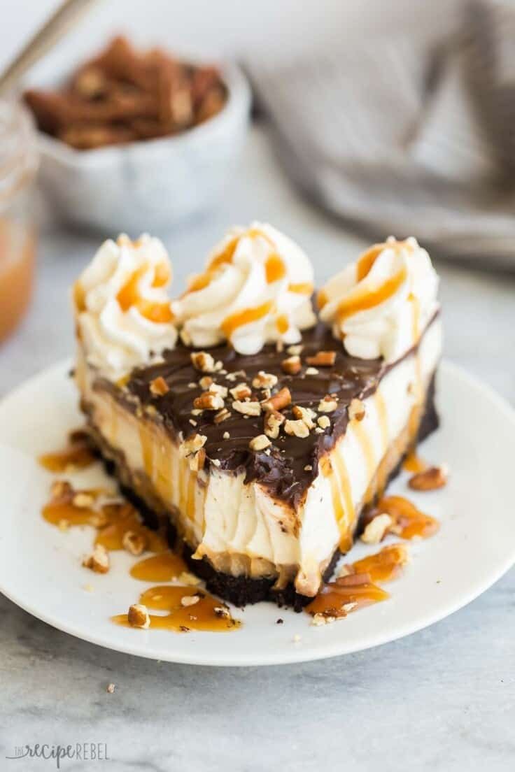 Part de cheesecake aux tortues servie avec un filet de caramel et des noix de pécan hachées.